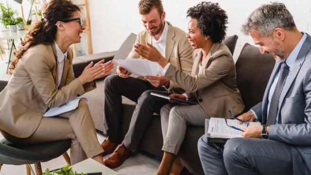 Co-workers discussing business travel expenses while seated on couches in a relaxed office space