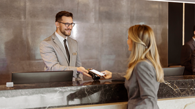 Female business traveller makes payment at hotel reception using smartphone