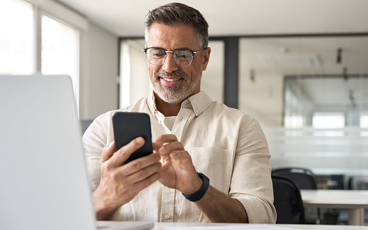 Business traveller sitting on a work desk, reviewing travel expenses on his phone